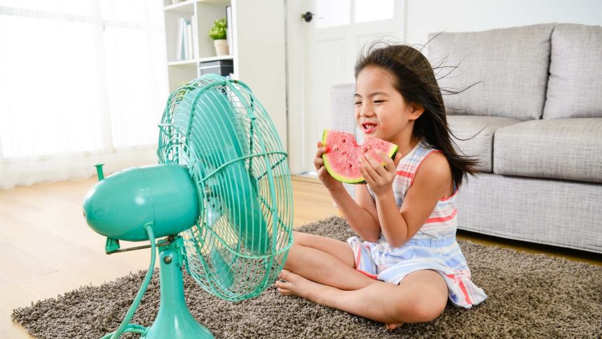 Une fille se rafraîchit devant un éventail avec une tranche de melon d'eau.