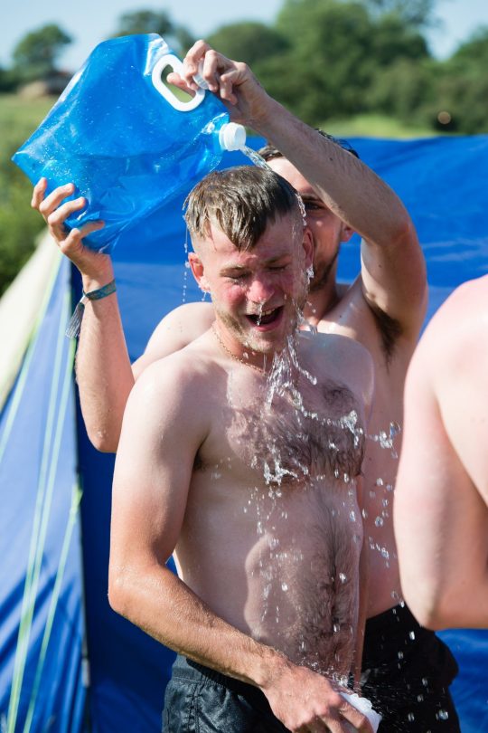 Les festivaliers versent de l'eau sur leur ami pour le refroidir et le laver le deuxième matin du festival par temps chaud et ensoleillé - l'atmosphère du festival le deuxième matin du festival Festival de Glastonbury