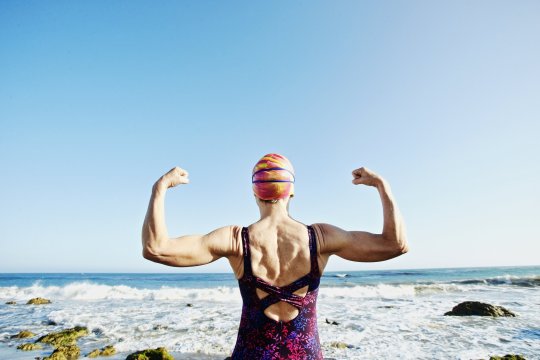 Femme caucasienne âgée, fléchissant ses muscles sur la plage
