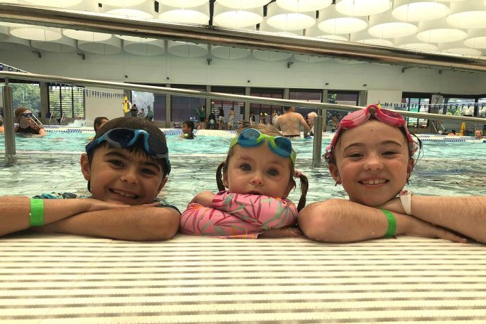 Gympie atteint 41C Trois enfants souriant sur le côté d'une piscine publique intérieure