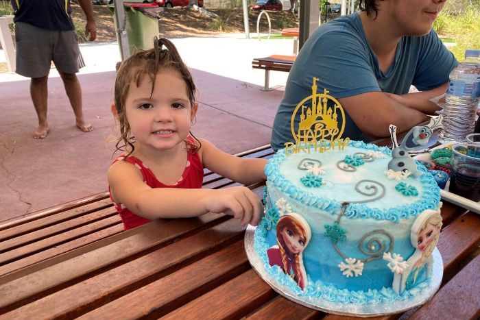 Chaleur d'anniversaire Une petite fille encore mouillée de nager assis à une table de pique-nique avec un gâteau d'anniversaire bleu