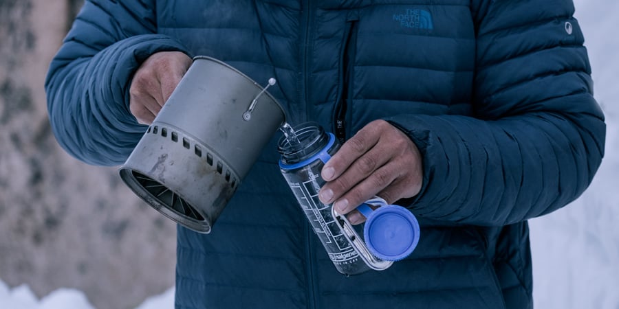 un randonneur versant de l'eau chaude dans une bouteille d'eau